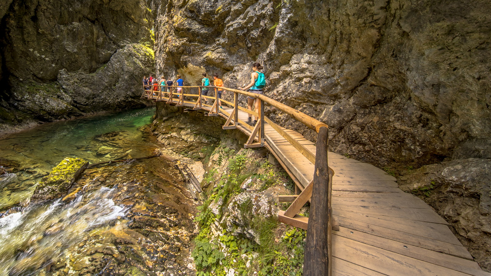 Soteska vintgar gorge with tourists walking on boardwalk along river on sunny day