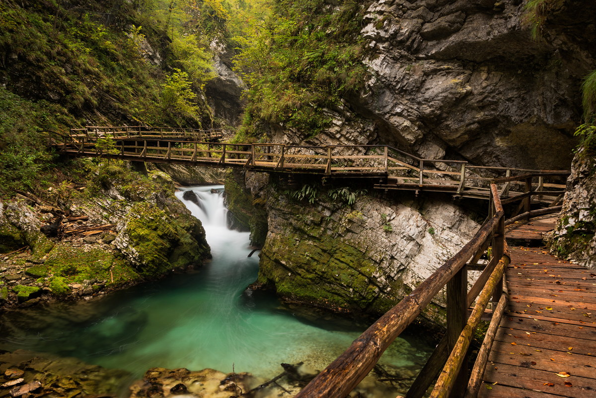 Wooden walkway through Vintgar Gorge canyon with a bridge over the emerald water of the stream in the mountains near Bled in Slovenia.