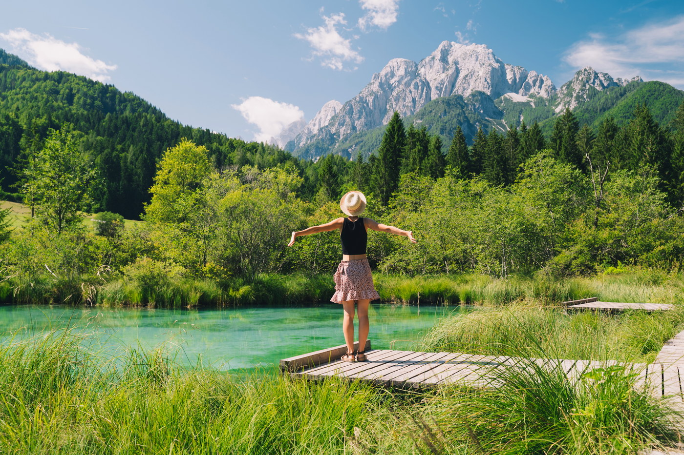 People in nature. Tourist woman with raised arms up in green nature background. View on Zelenci (into English means - green) natural reserve in Slovenia, Europe. Travel, Freedom, Lifestyle concept.